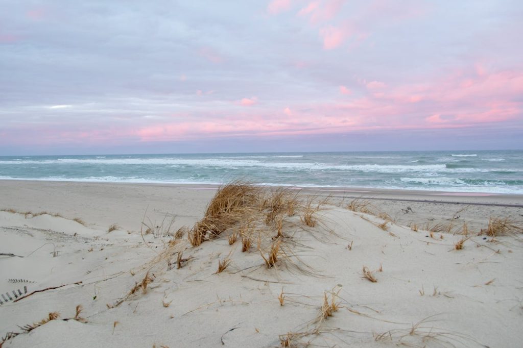 Peaceful sandy beach in Provincetown, MA with pink dawn sky and ocean waves.